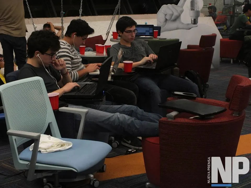 Students in headphones coding on laptops from lounge chairs, with red plastic cups nearby, at Hackathon 7