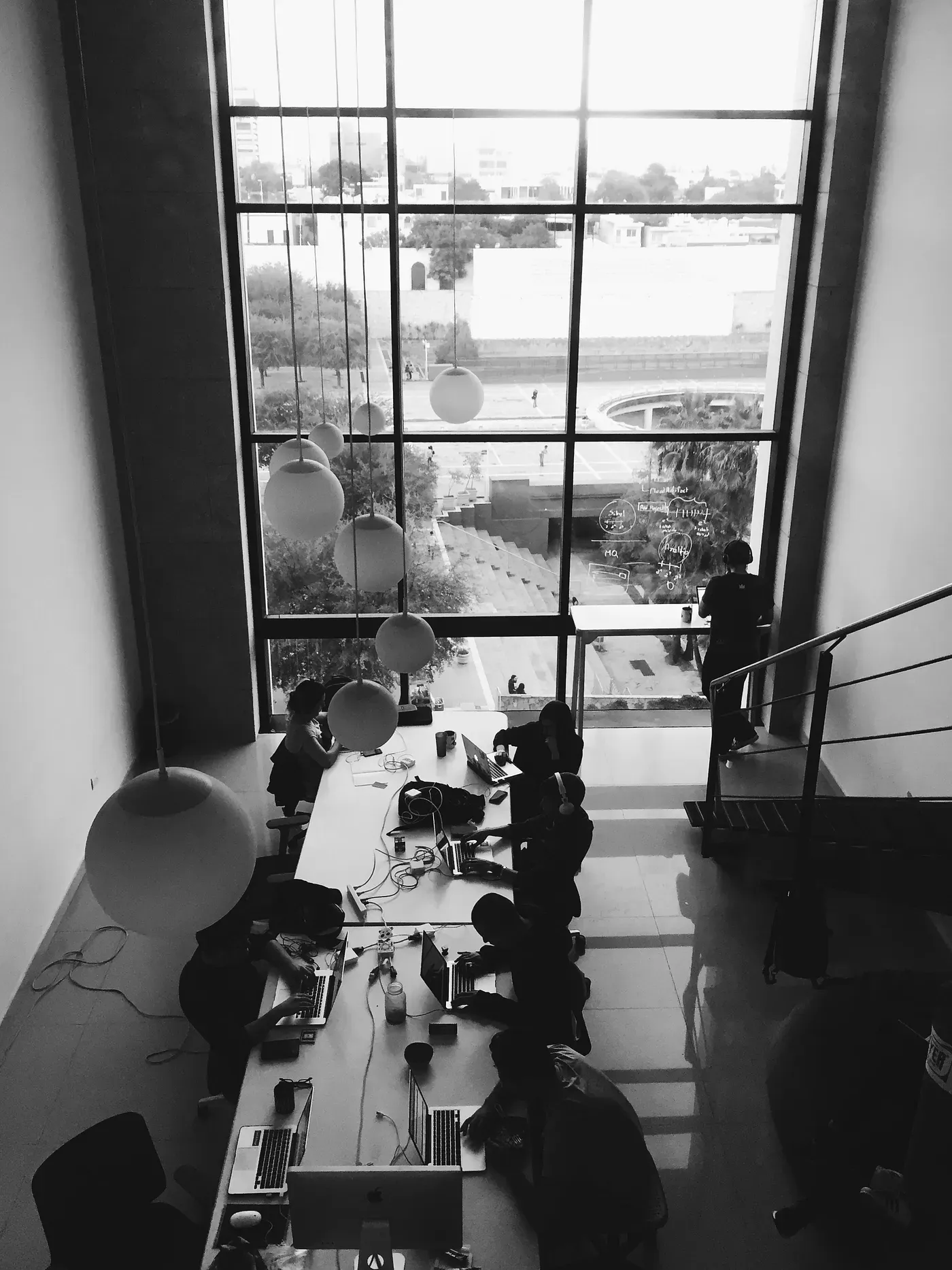Black-and-white overhead view of the Icalia Labs team working at a long shared desk in front of a tall window